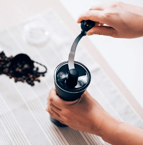 The Hario Mini Slim Coffee Grinder on a table being held.